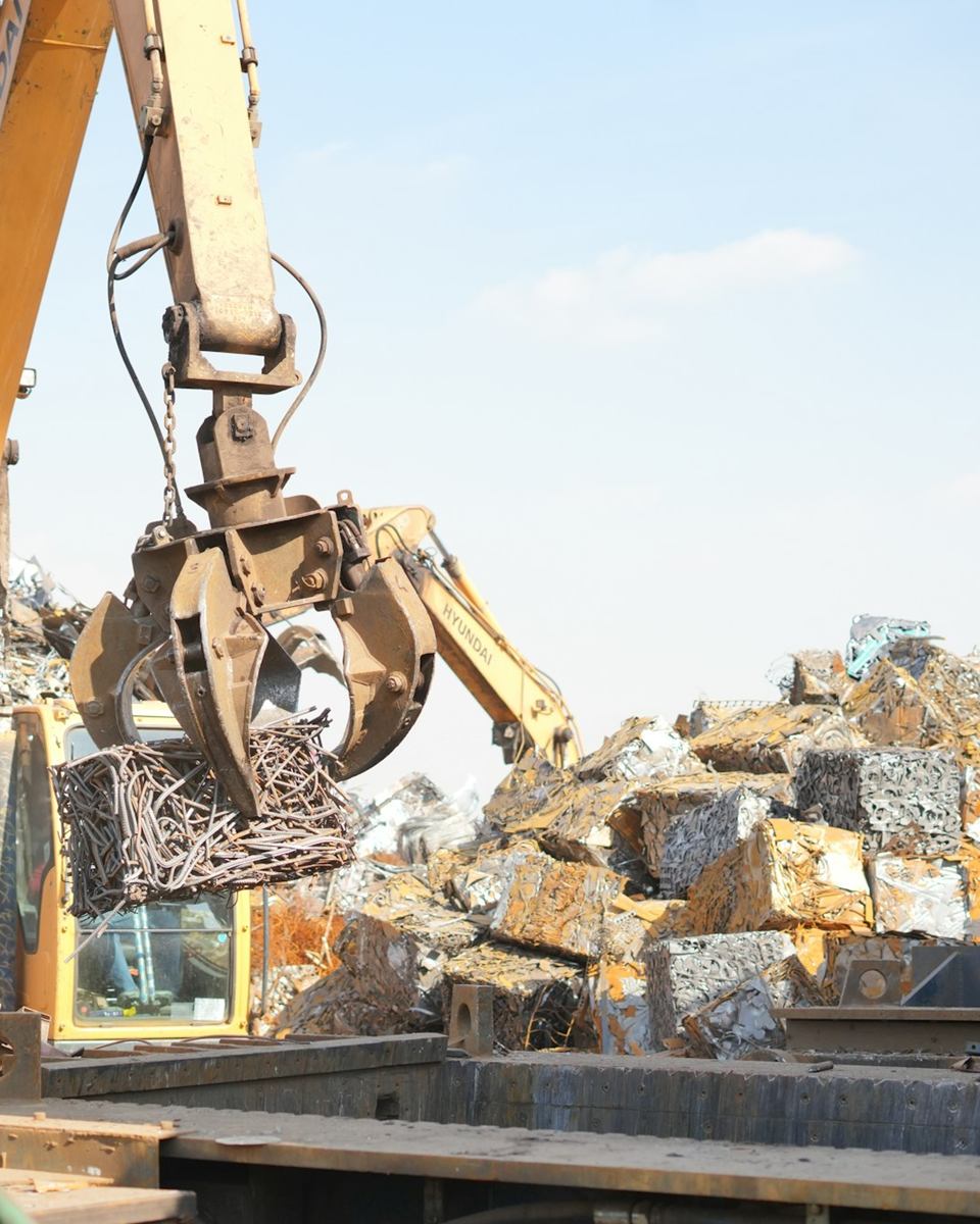 Grappin de manutention soulevant une balle de ferraille dans un parc de recyclage